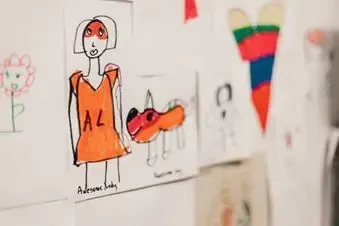 A child 's drawing of a woman in an orange dress is hanging on a wall.