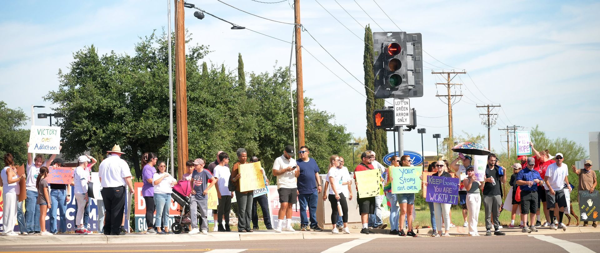 Crowd of people holding signs at a street intersection near a traffic light, suggesting a protest or march