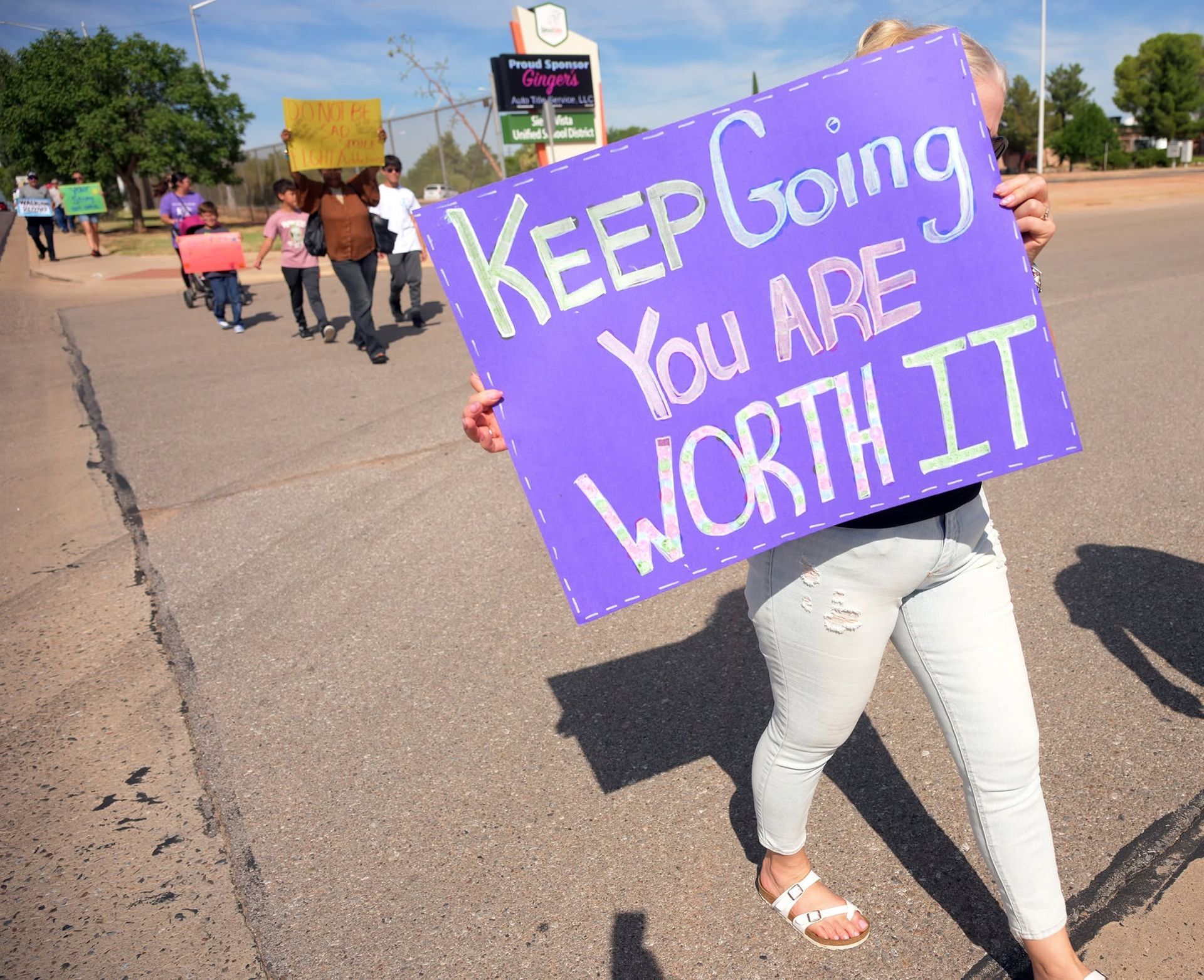 Protester holding purple sign reading “KEEP going You are WORTH IT” on a street during a march