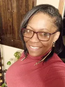 A woman wearing glasses and a red turtleneck is smiling for the camera.