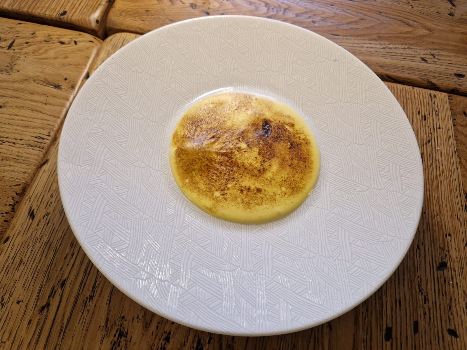 Une assiette blanche surmontée d'une crêpe sur une table en bois.