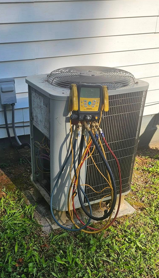 Outdoor HVAC unit with a yellow gauge manifold and colorful hoses attached against a house wall