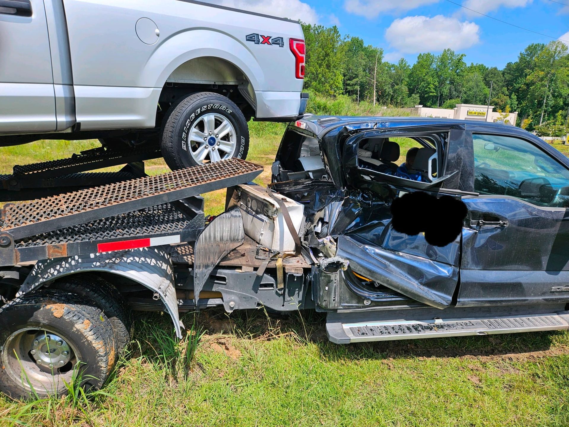 White pickup on a trailer after a wreck with a badly damaged black car beside it in a grassy field