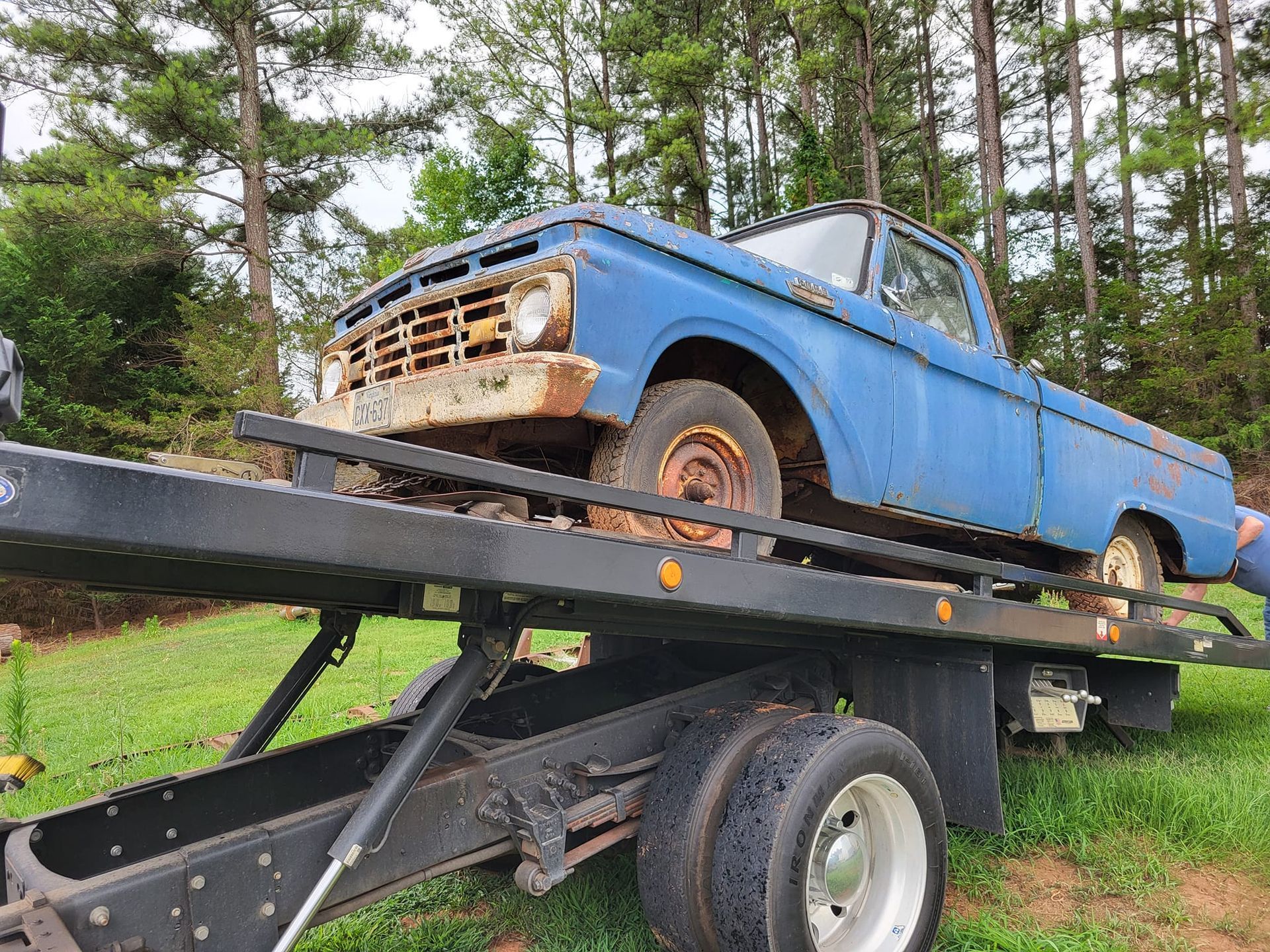 Blue rusty pickup on a tow truck in a wooded area