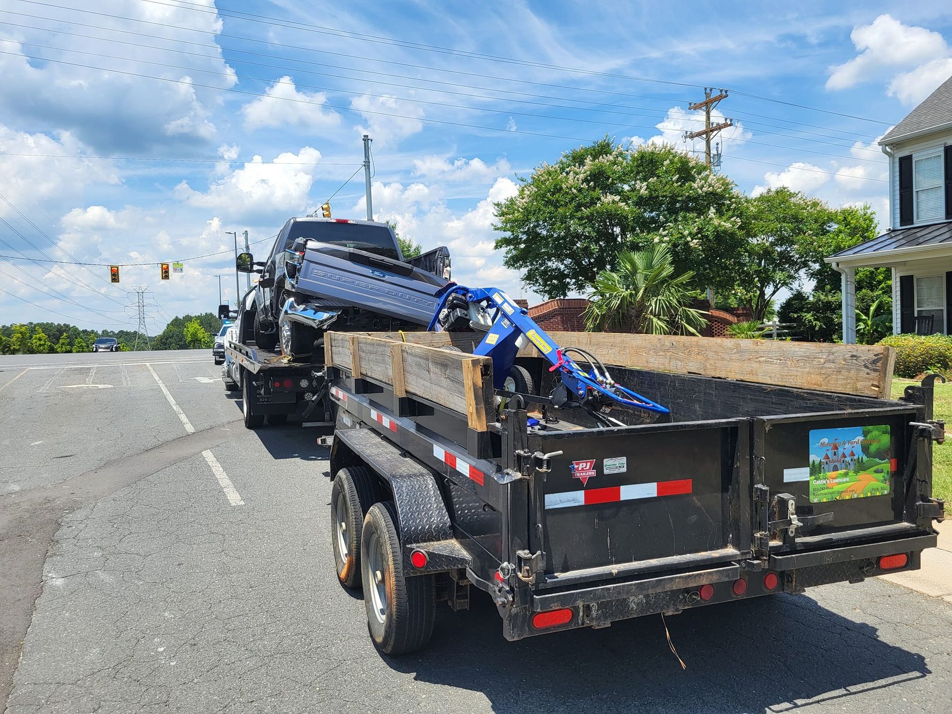 Black trailer loaded with debris on a roadside under a bright blue sky.