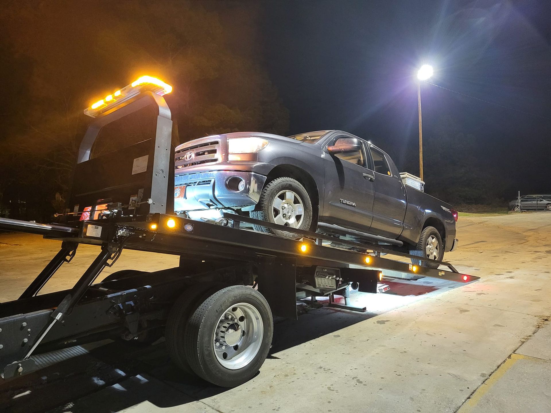 Tow truck hauling a damaged gray pickup at night on a roadside
