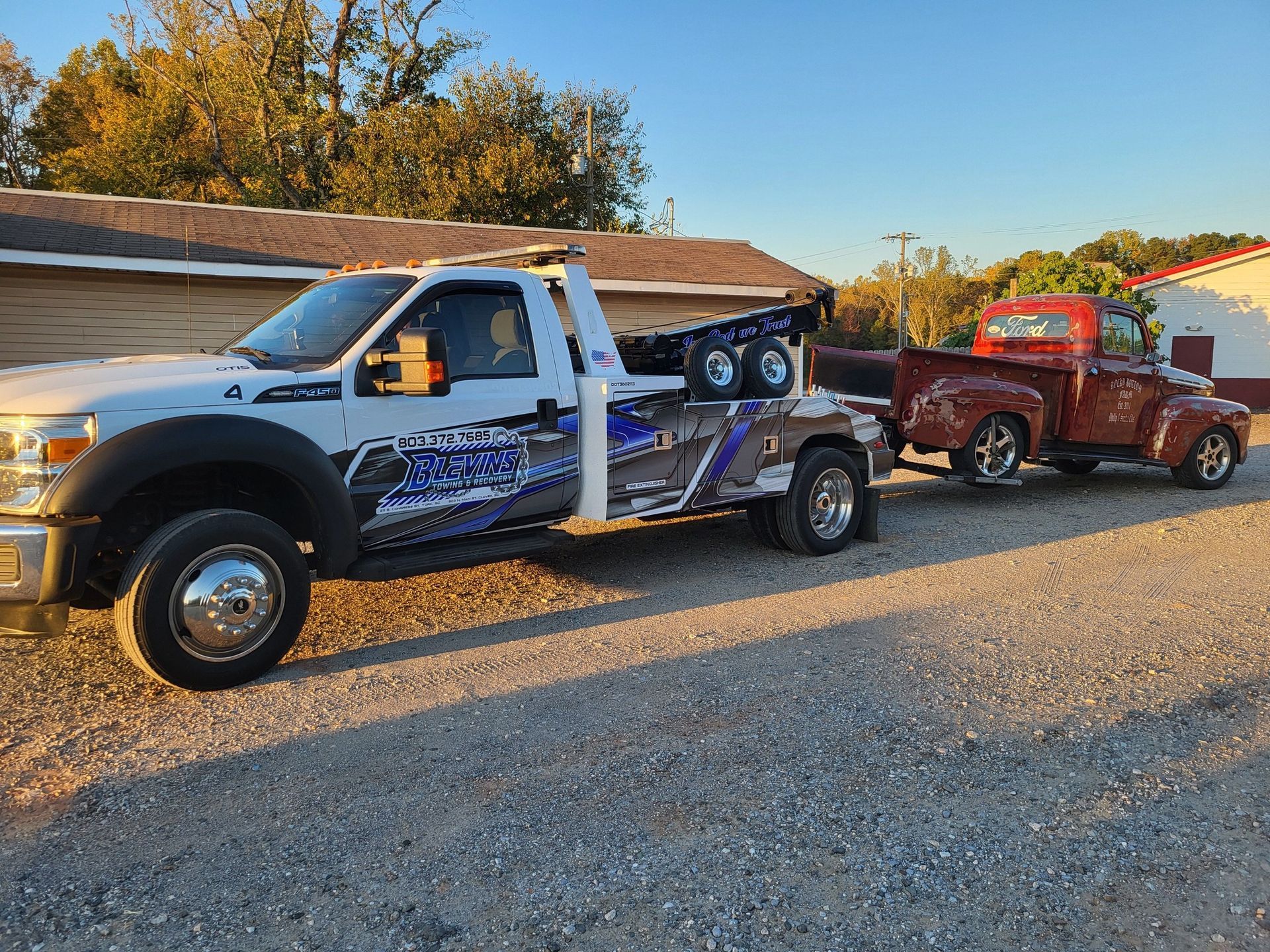 Two damaged tow trucks parked on a gravel road at sunset, one silver and one red