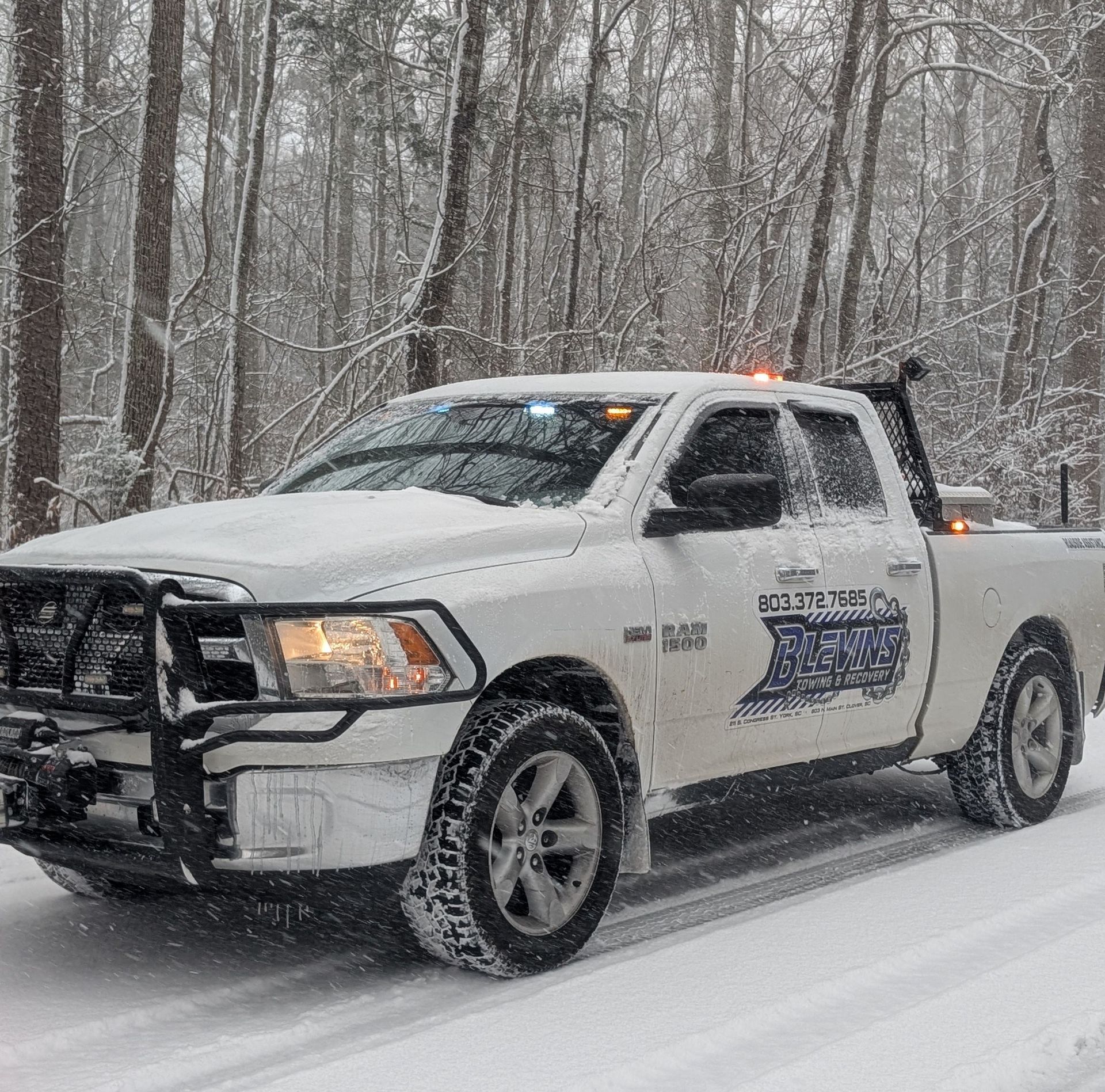 White pickup truck driving through snowy forest road in falling snow