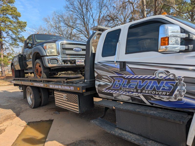 Tow truck carrying a dark pickup with Dlevins Towing and Recovery branding on the side