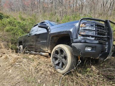 Black pickup truck stuck off-road on a muddy hillside, front end tilted in brush.