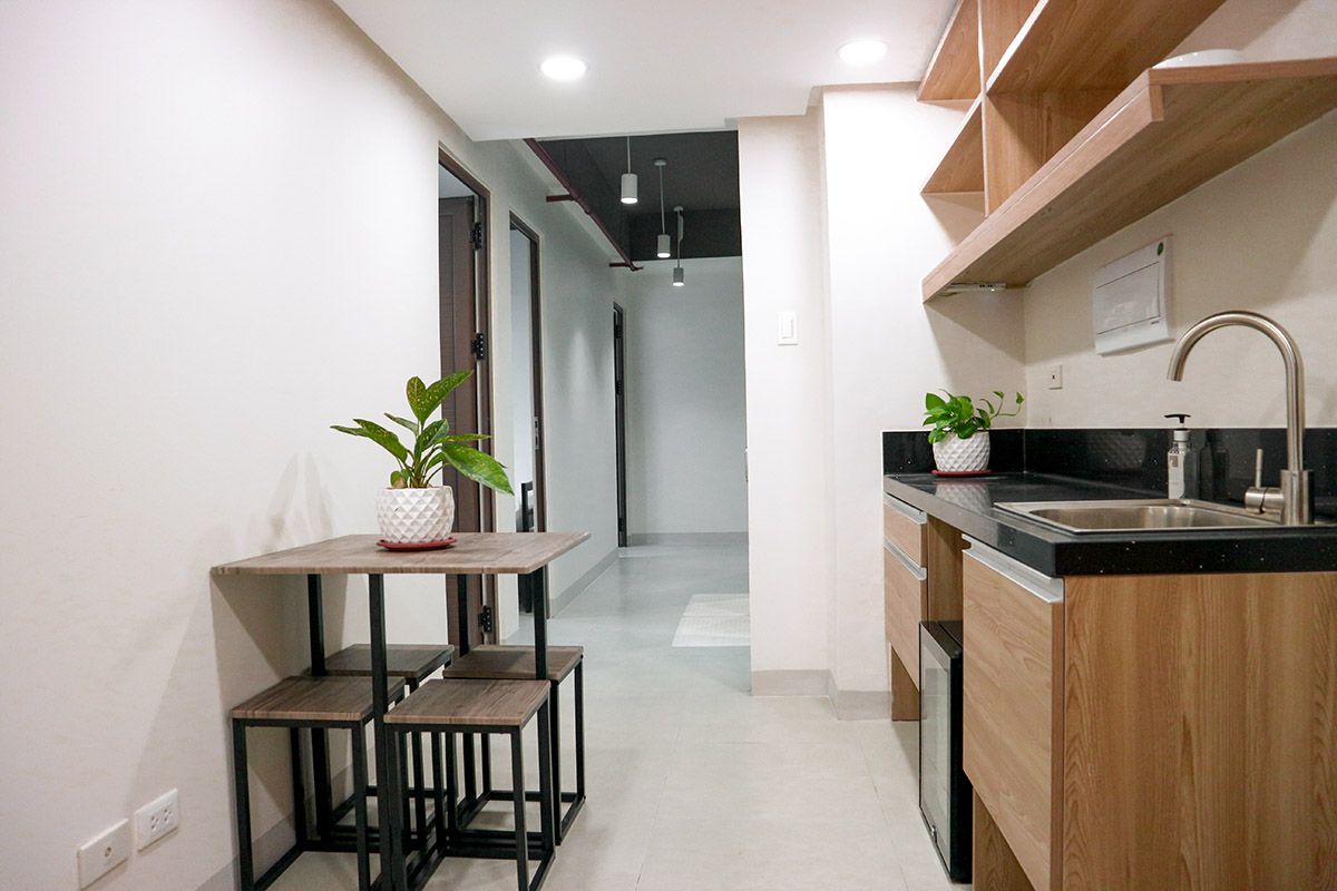 Small kitchen and dining area in a hallway, featuring a table, stools, cabinets, and a sink.