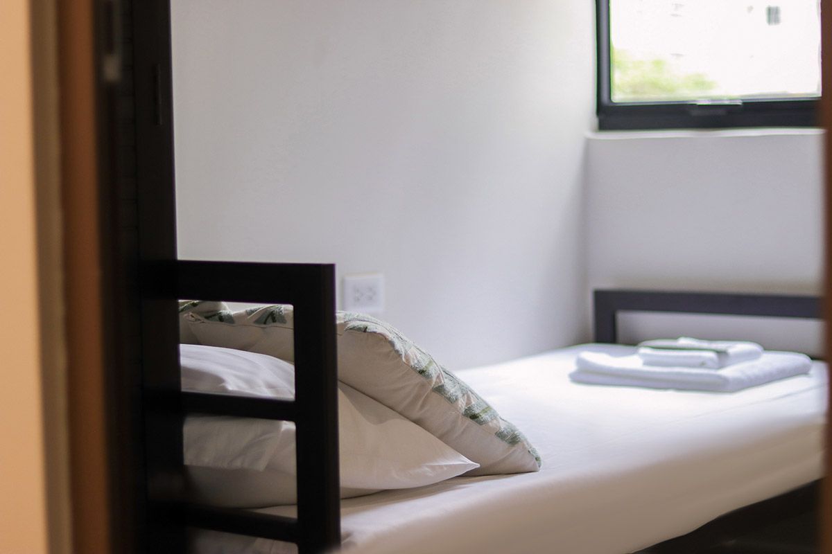 A small, tidy bedroom with a single bed and window. White linens and a pillow are on the bed.