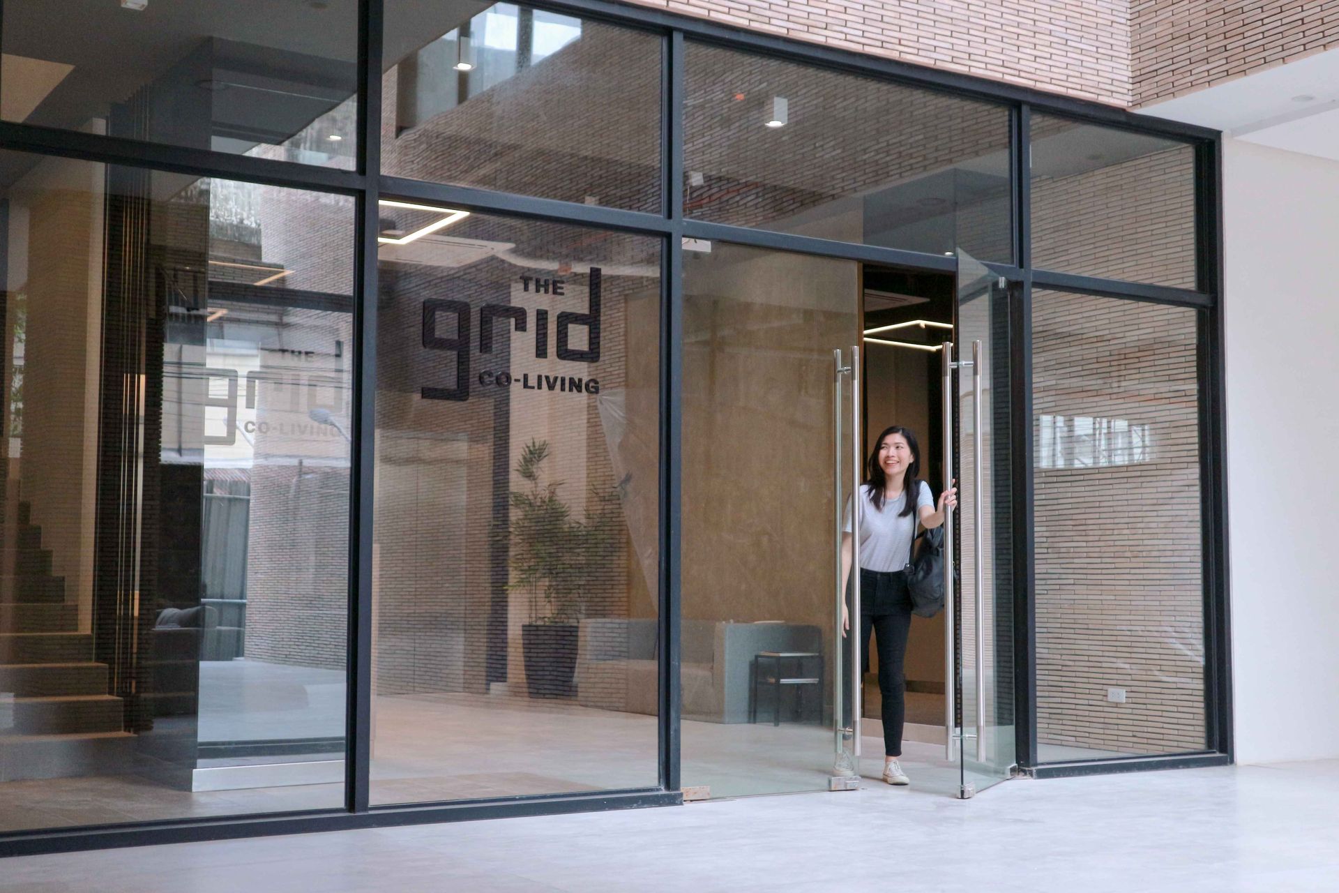 Person standing in a glass storefront entrance with the word “grid” on the wall inside.