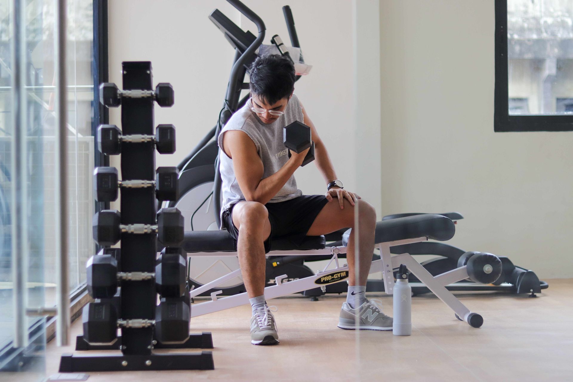 A man is sitting on a bench in a gym holding a dumbbell.