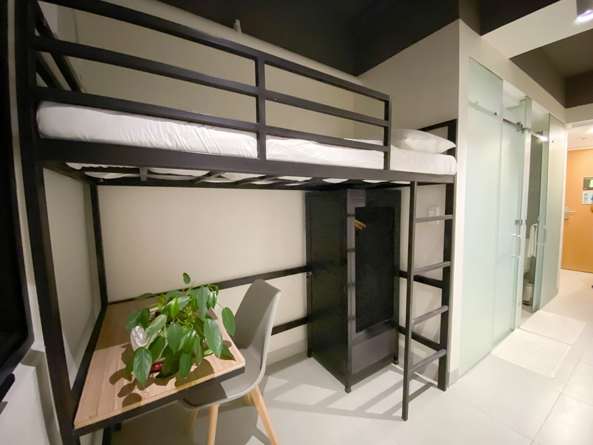 Black bunk bed with desk, chair, and wardrobe in a small room.