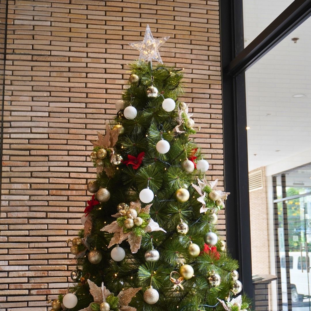 Decorated Christmas tree with white and gold ornaments, topped with a star, against a brick wall.
