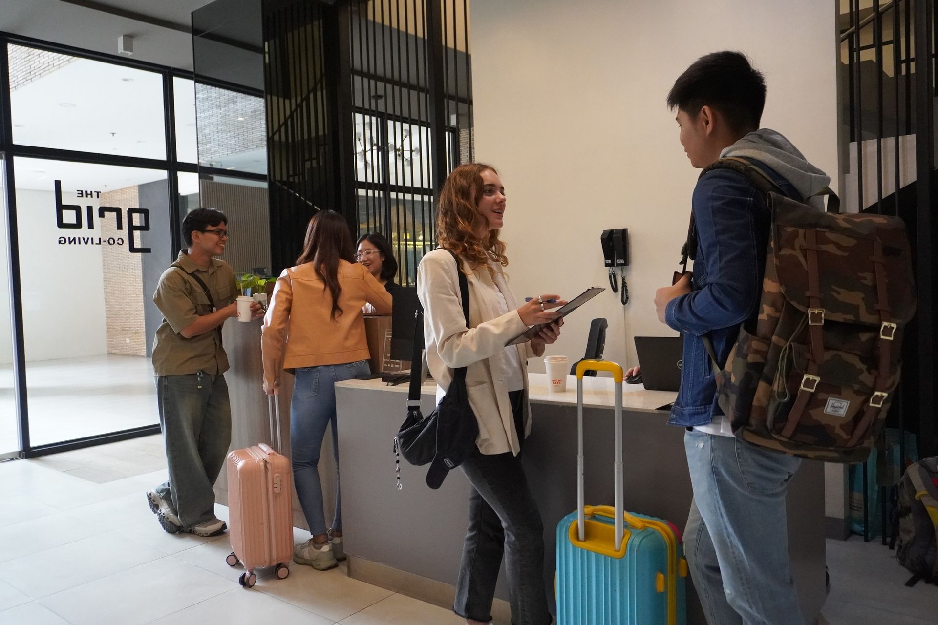 People checking in at a hotel front desk. Suitcases, smiles, and the hotel logo are visible.