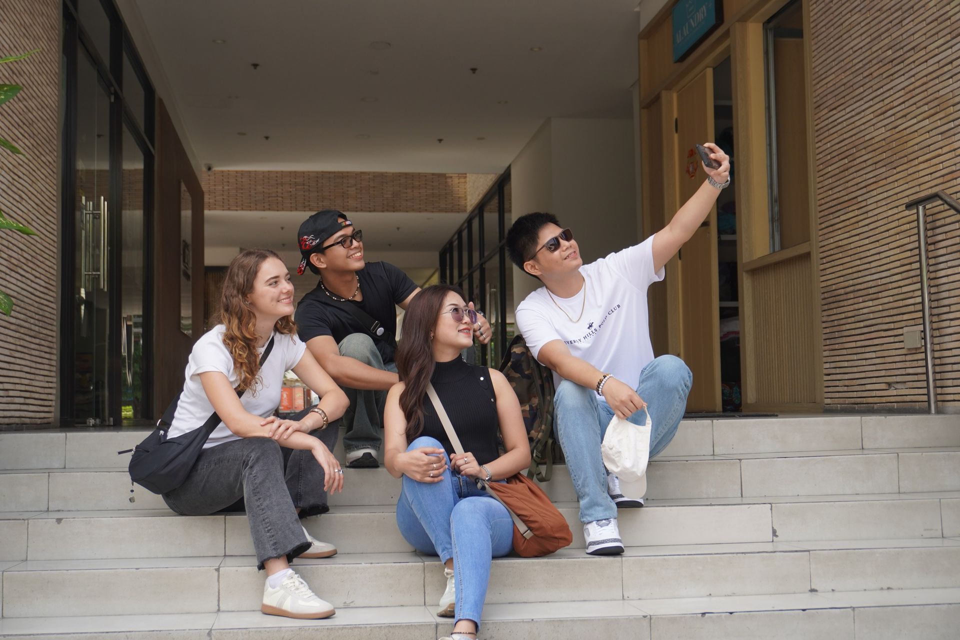 Four people taking a selfie on outdoor steps; building in background.