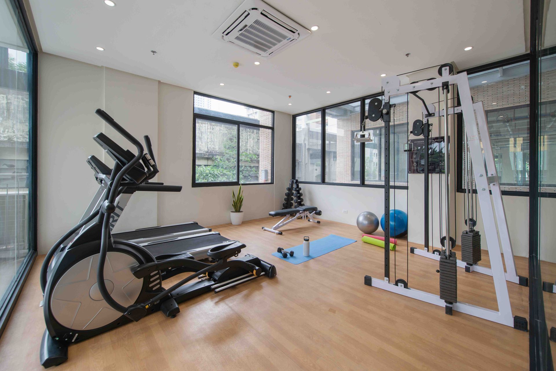 Modern home gym with treadmill, cable machine, yoga mat, and exercise ball on a wood floor