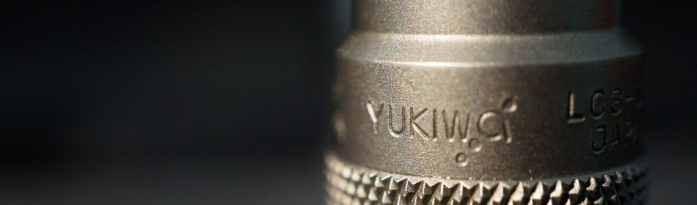 Close-up of a metal microphone with textured grip and engraved lettering, softly lit against a dark background
