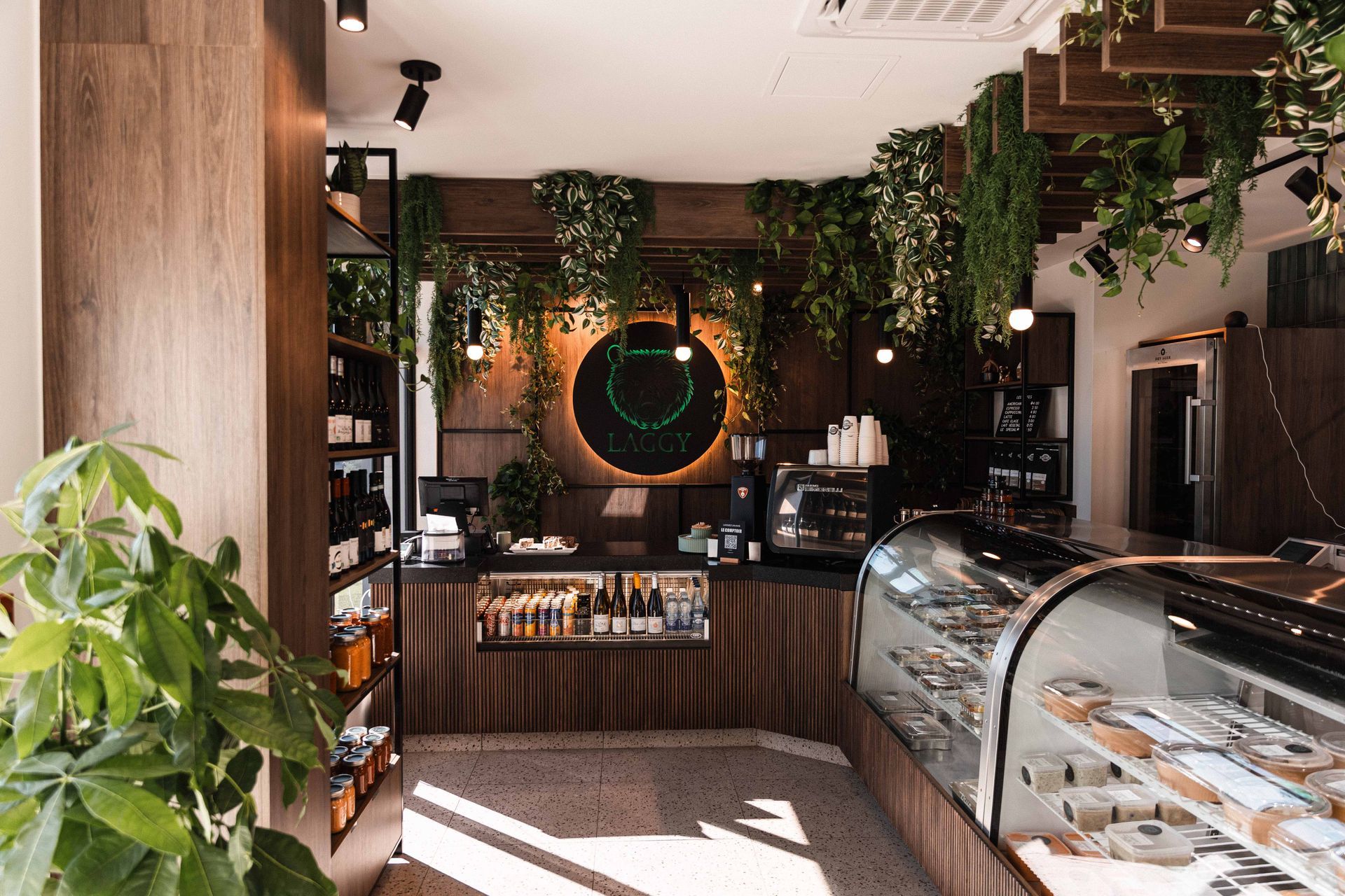 Intérieur d'un café avec des boiseries, une vitrine et des plantes vertes.