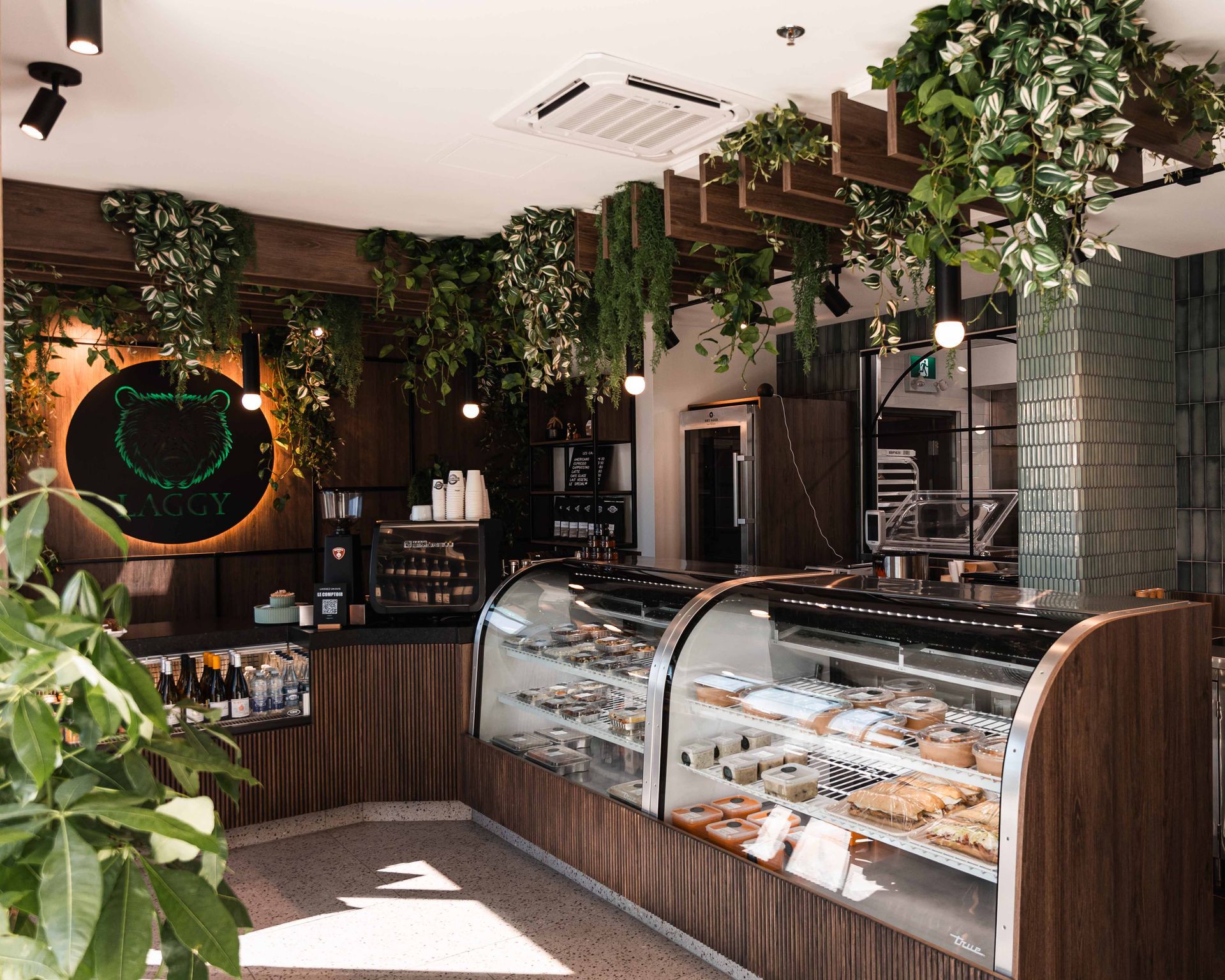 Intérieur d'un café avec présentoir de pâtisseries, plantes et éléments en bois.