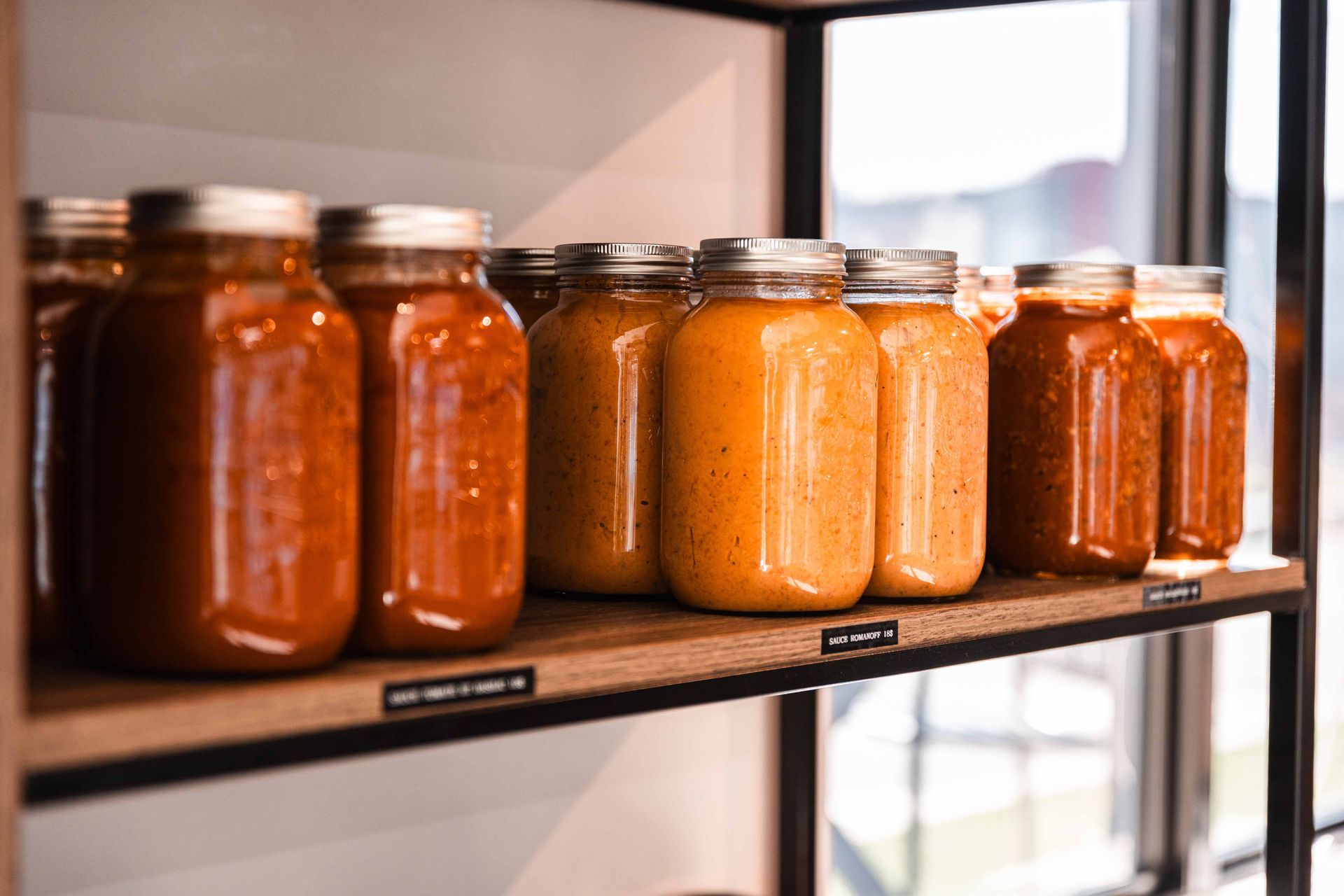 Des bocaux de sauces orange et rouges de différentes couleurs sont posés sur une étagère en bois dans un magasin.