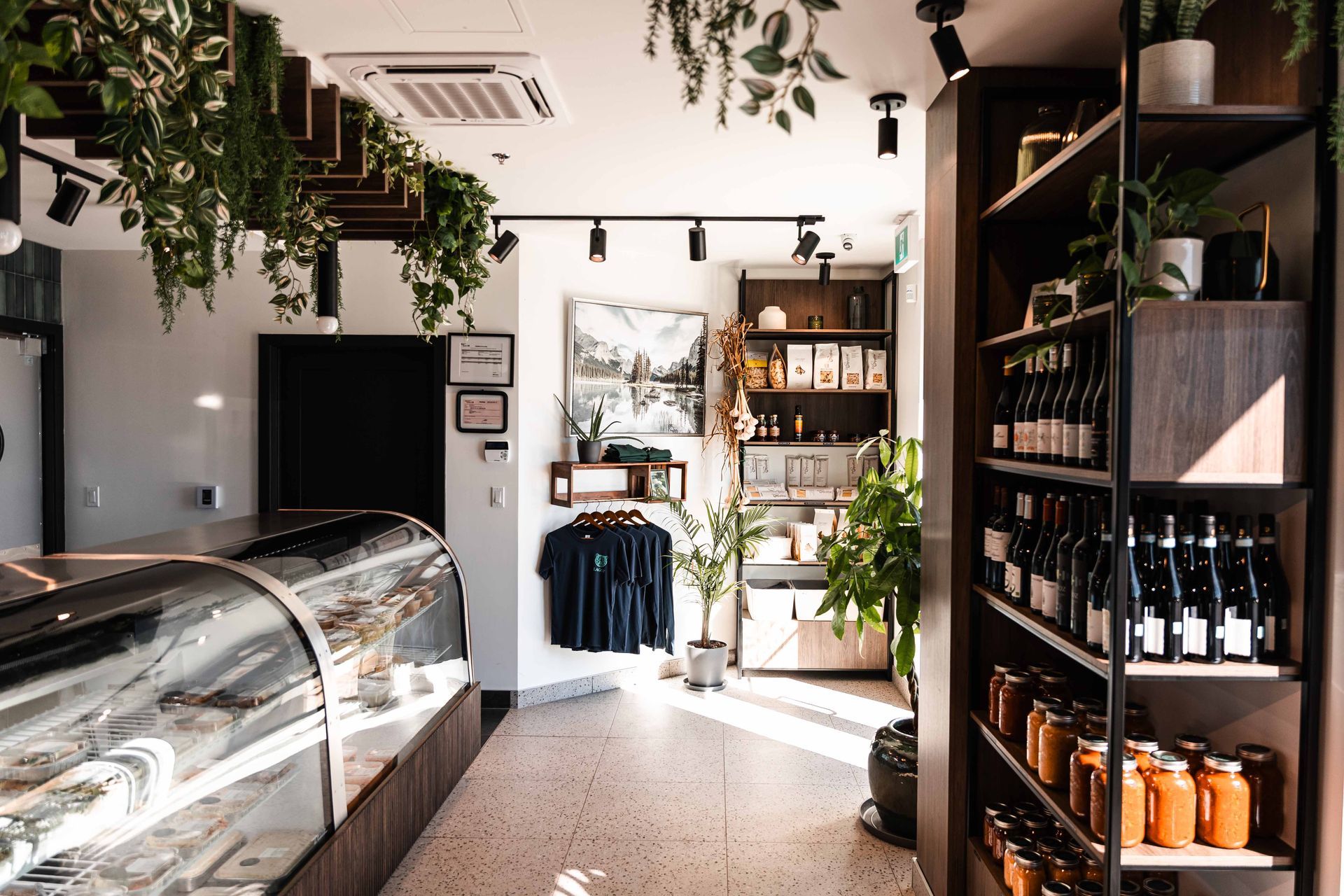 Intérieur d'un magasin avec une vitrine, des étagères de bouteilles et des plantes suspendues.