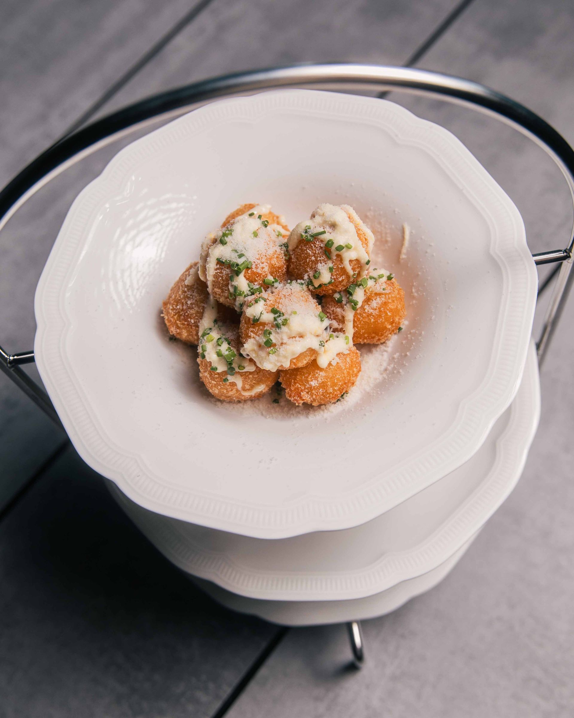 Boulettes de pommes de terre frites nappées de sauce blanche et parsemées d'herbes, servies sur une assiette blanche.