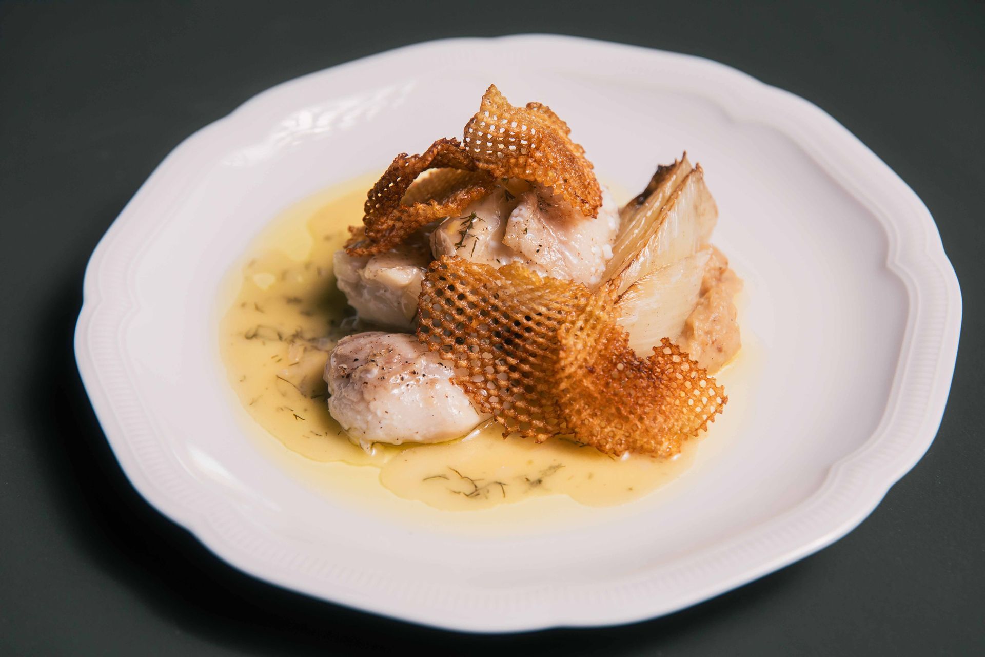 Plat de fruits de mer servi sur une assiette avec une sauce jaune, garni d'une couche croustillante en forme de dentelle.
