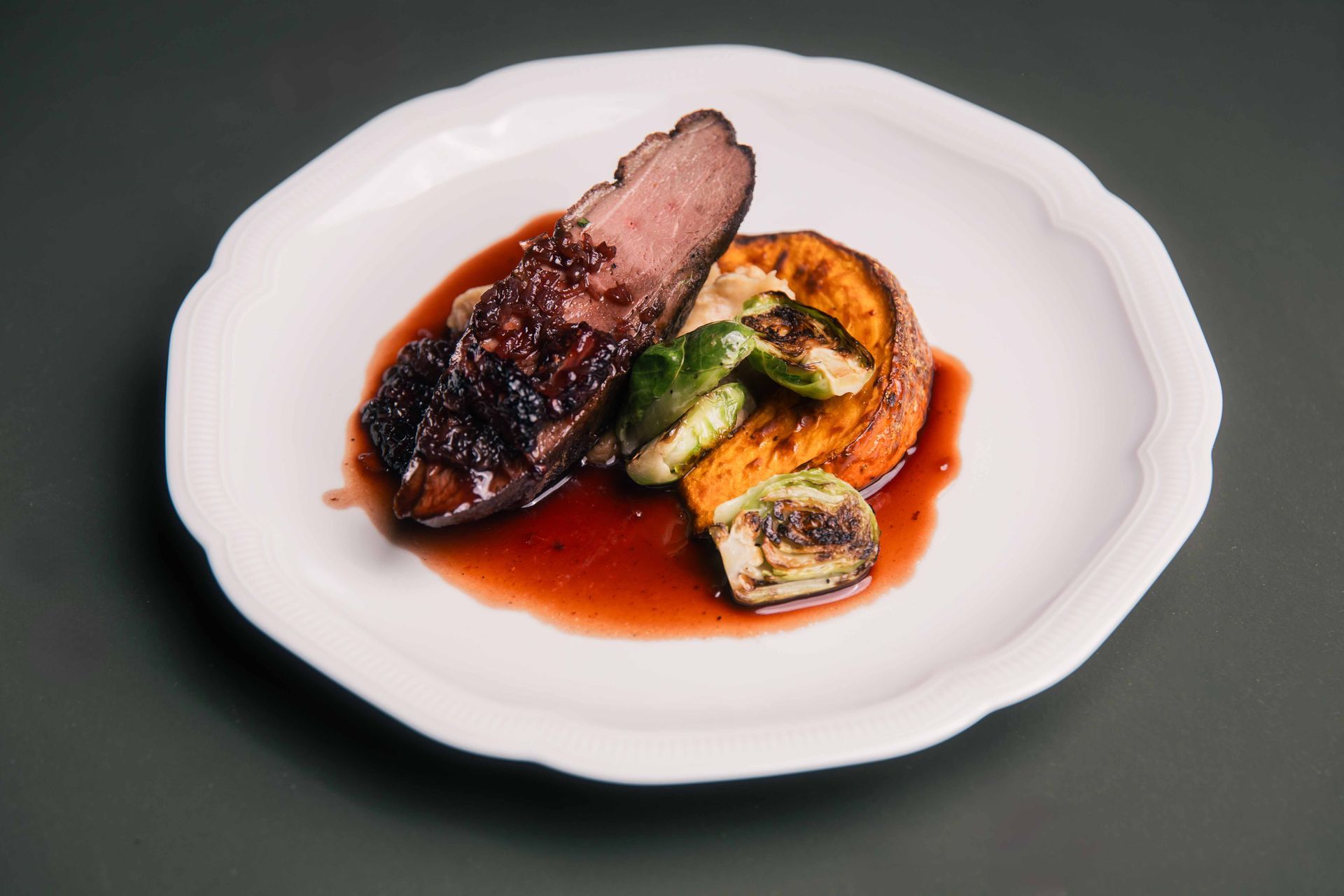 Magret de canard nappé de sauce glacée, accompagné de patate douce et de choux de Bruxelles, servi sur une assiette blanche.