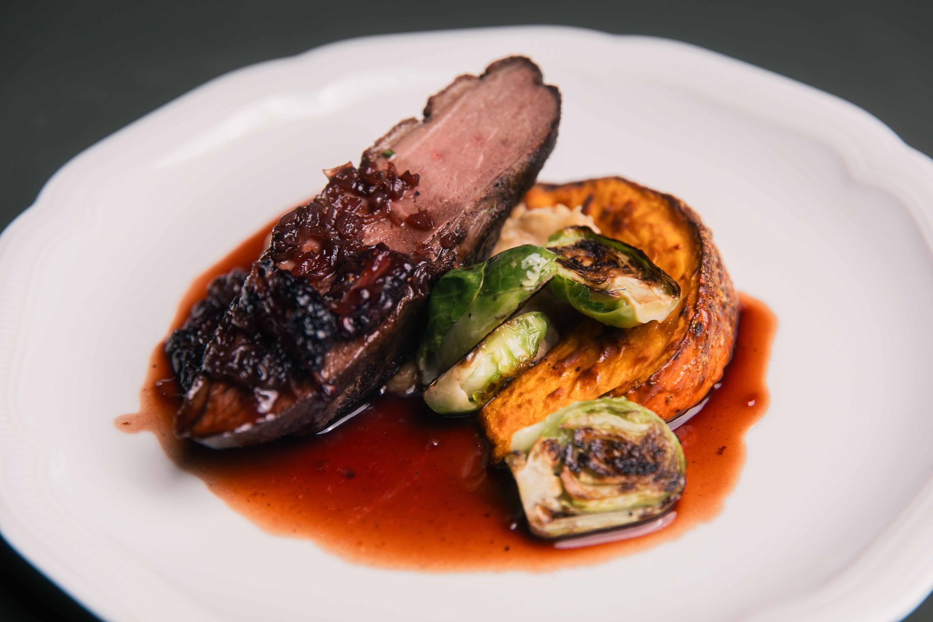 Magret de canard en sauce, patate douce rôtie et choux de Bruxelles sur une assiette blanche.
