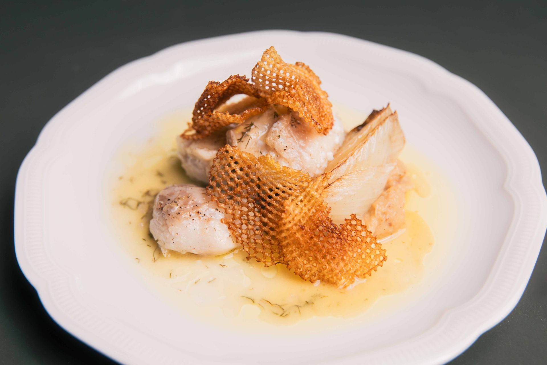 Noix de Saint-Jacques poêlées, garnies d'un treillis croustillant, servies sur une assiette blanche.