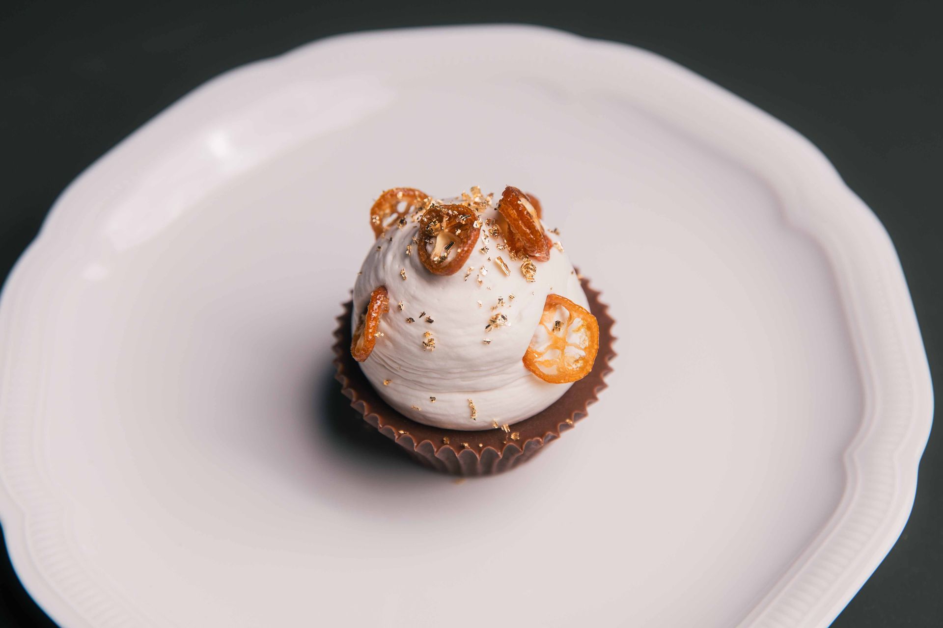 Cupcake sur une assiette blanche avec glaçage blanc, coupelle en chocolat et garnitures dorées.