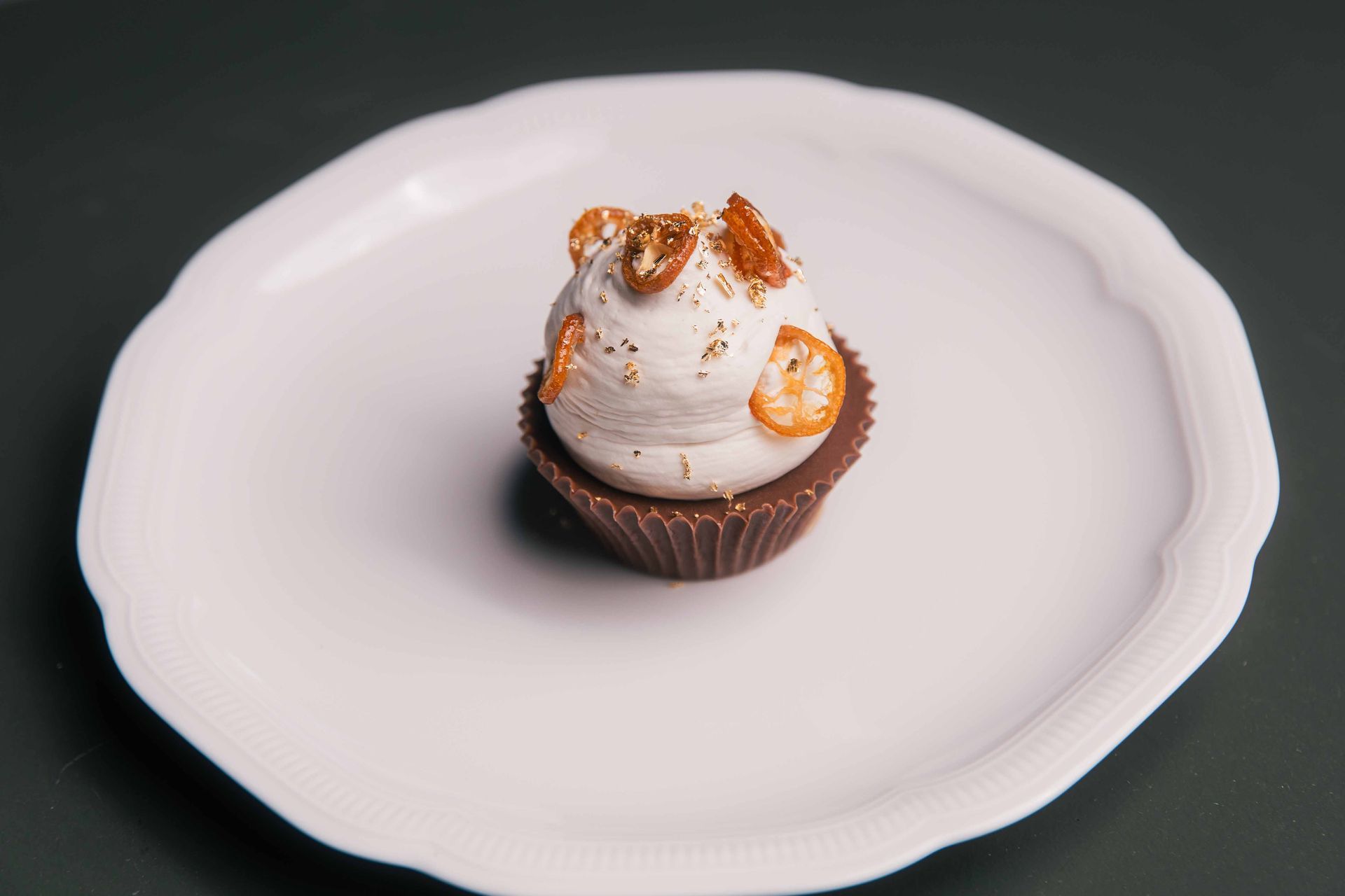 Un petit dessert : meringue sur une coupelle en chocolat, garnie de tranches d'orange, sur une assiette blanche irrégulière.