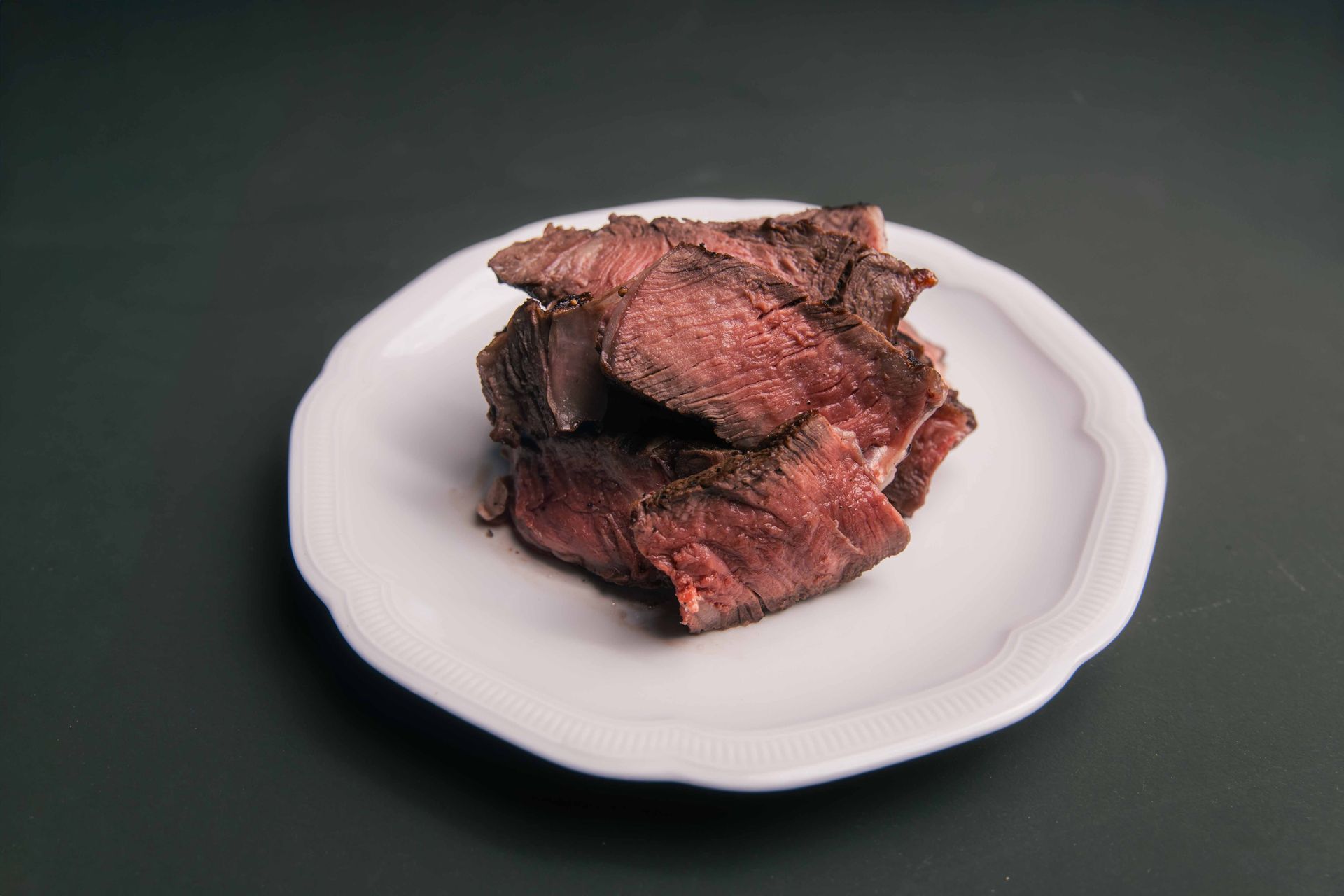 Tranches de viande cuite sur une assiette blanche, sur fond sombre.