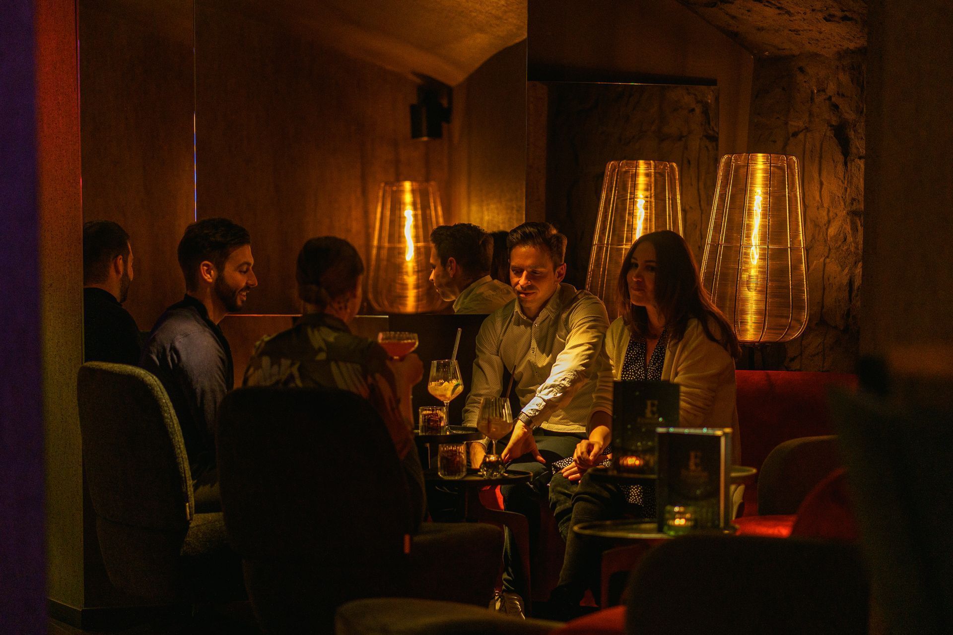 Menschen sitzen an einem schwach beleuchteten Restauranttisch bei warmem, bernsteinfarbenem Licht von Lampen und Getränken.