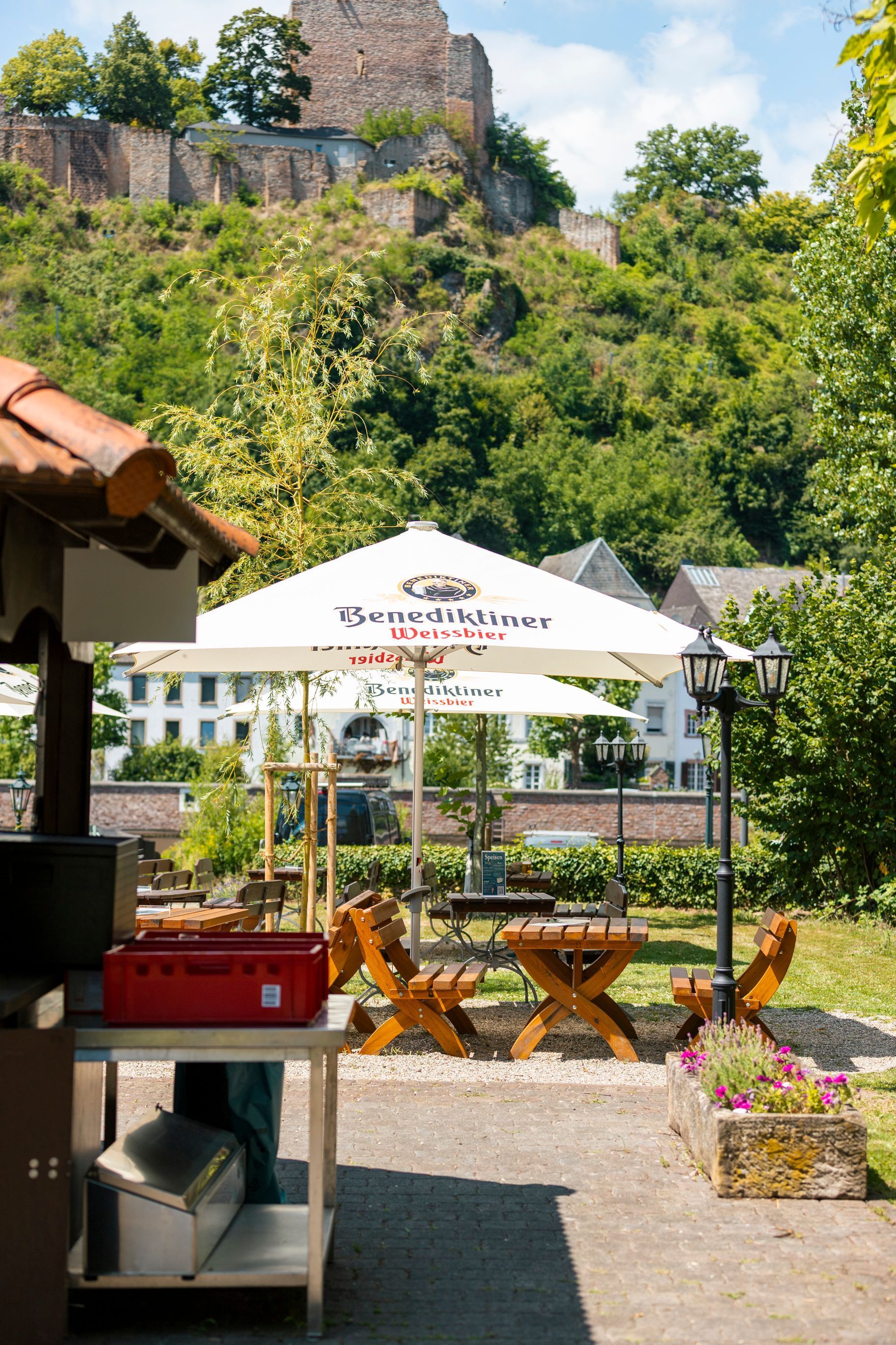 Sitzplätze im Freien unter einem weißen Sonnenschirm neben einem grünen Hügel und Steinruinen