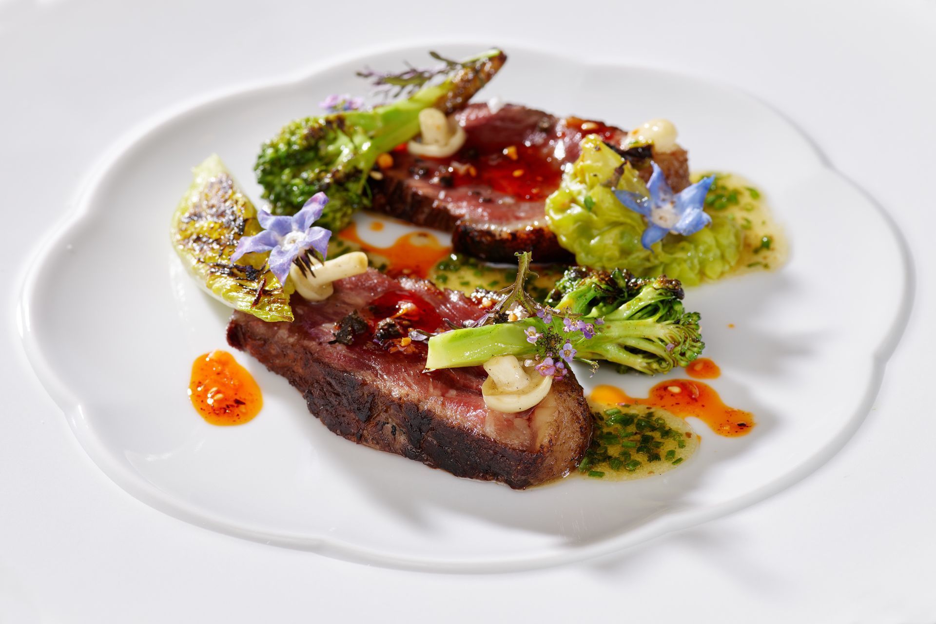Gourmet-Rindfleisch mit farbenfroher Sauce, Gemüse und essbaren Blüten auf einem weißen Teller angerichtet
