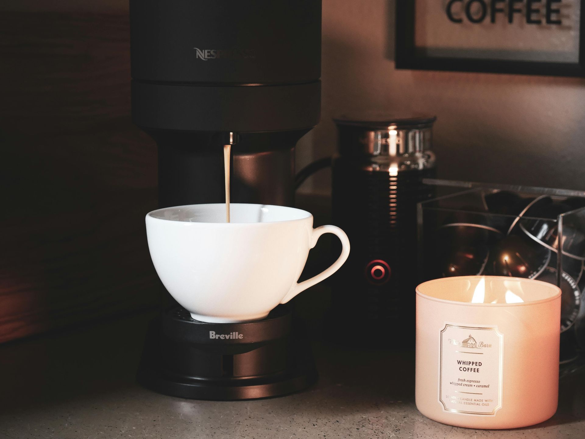 Eine Kaffeemaschine füllt Kaffee in eine weiße Tasse neben einer brennenden Kerze auf einer dunklen Theke.