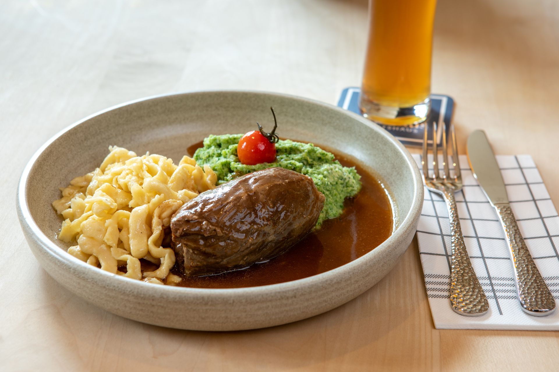 Steak mit Kartoffelpüree und grüner Soße auf einem Teller neben einem Orangensaft und Besteck.