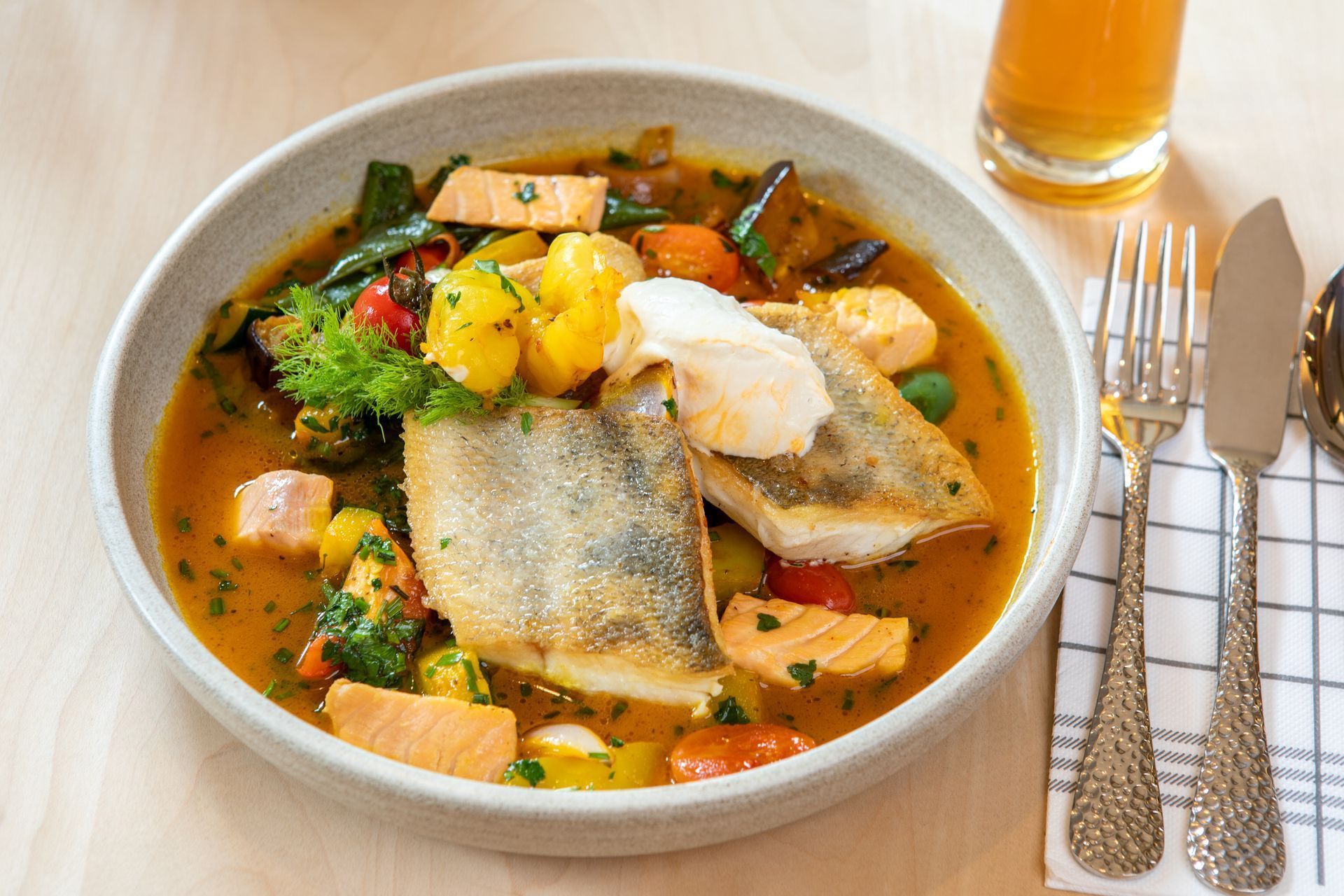 Fischeintopf in einer Schüssel mit Gemüse, Brot und einem Glas Orangensaft auf einem Tisch