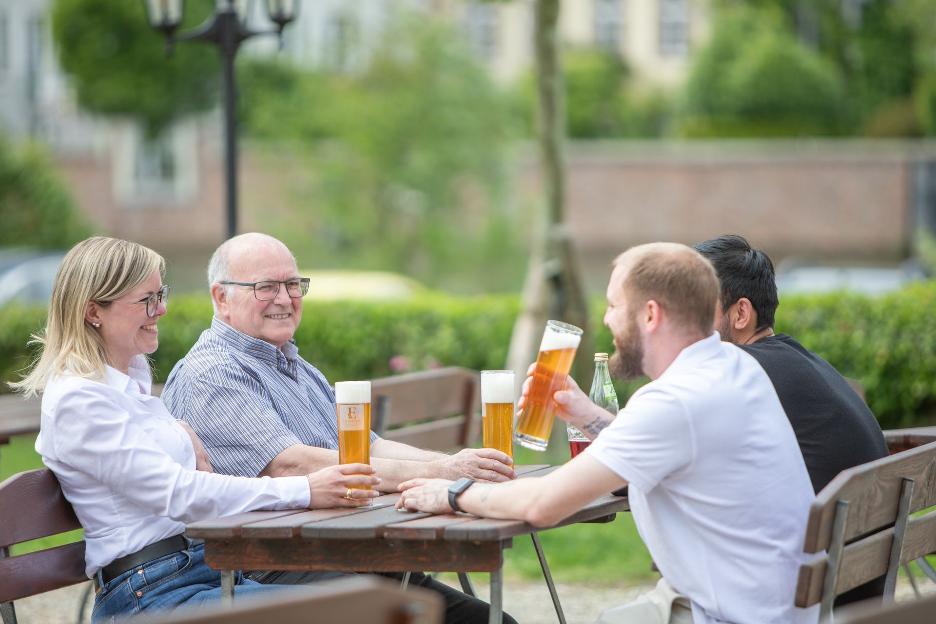 Vier Personen sitzen draußen an einem Terrassentisch, unterhalten sich und trinken Bier.