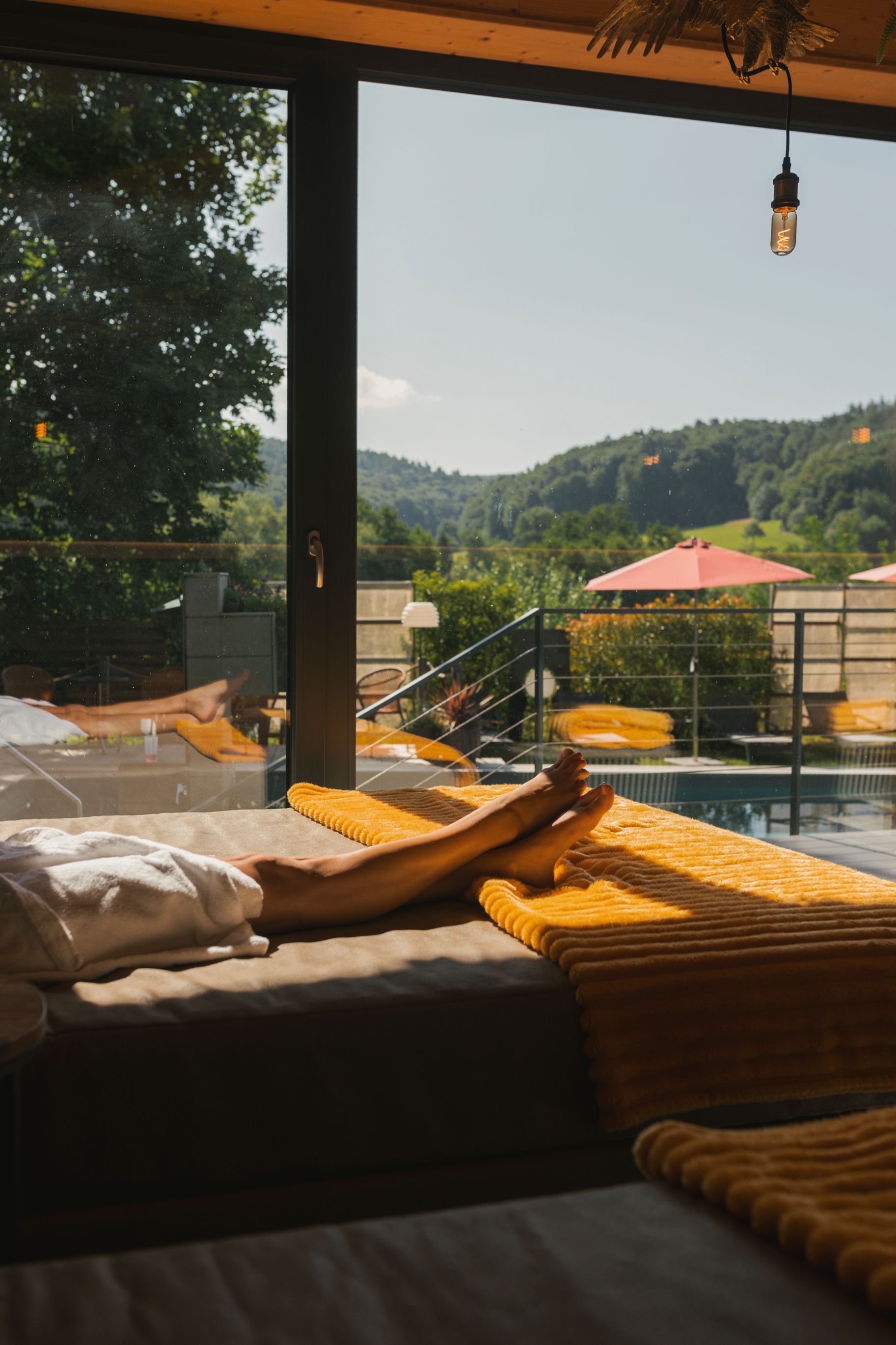 Gemütliche Lounge am Pool mit freiem Blick auf grüne Hügel und einem rosafarbenen Sonnenschirm im warmen Sonnenlicht