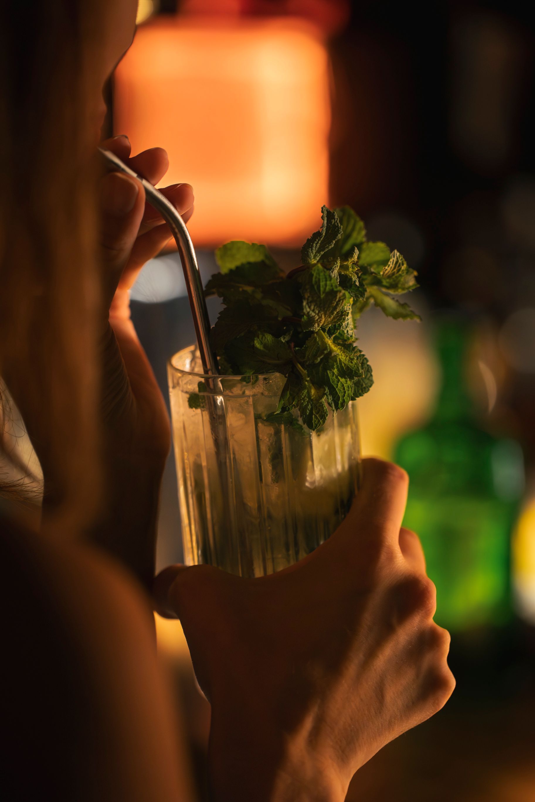 Eine Hand hält einen Cocktail mit Minze und Strohhalmen in einer schwach beleuchteten Bar.