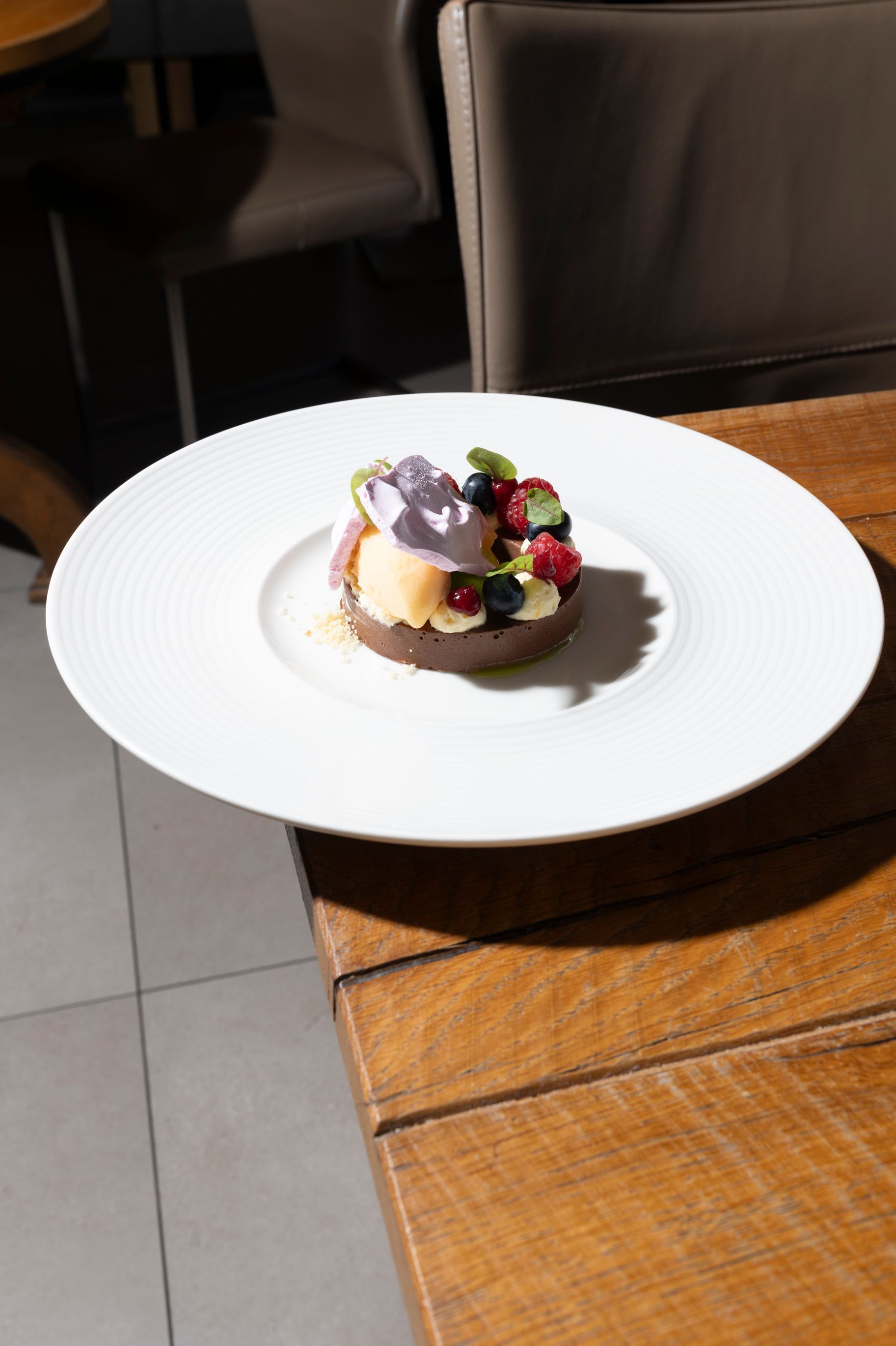 Ein kleiner Dessertteller mit Beeren und Schokoladengarnitur auf einem weißen Teller an einem Holztisch