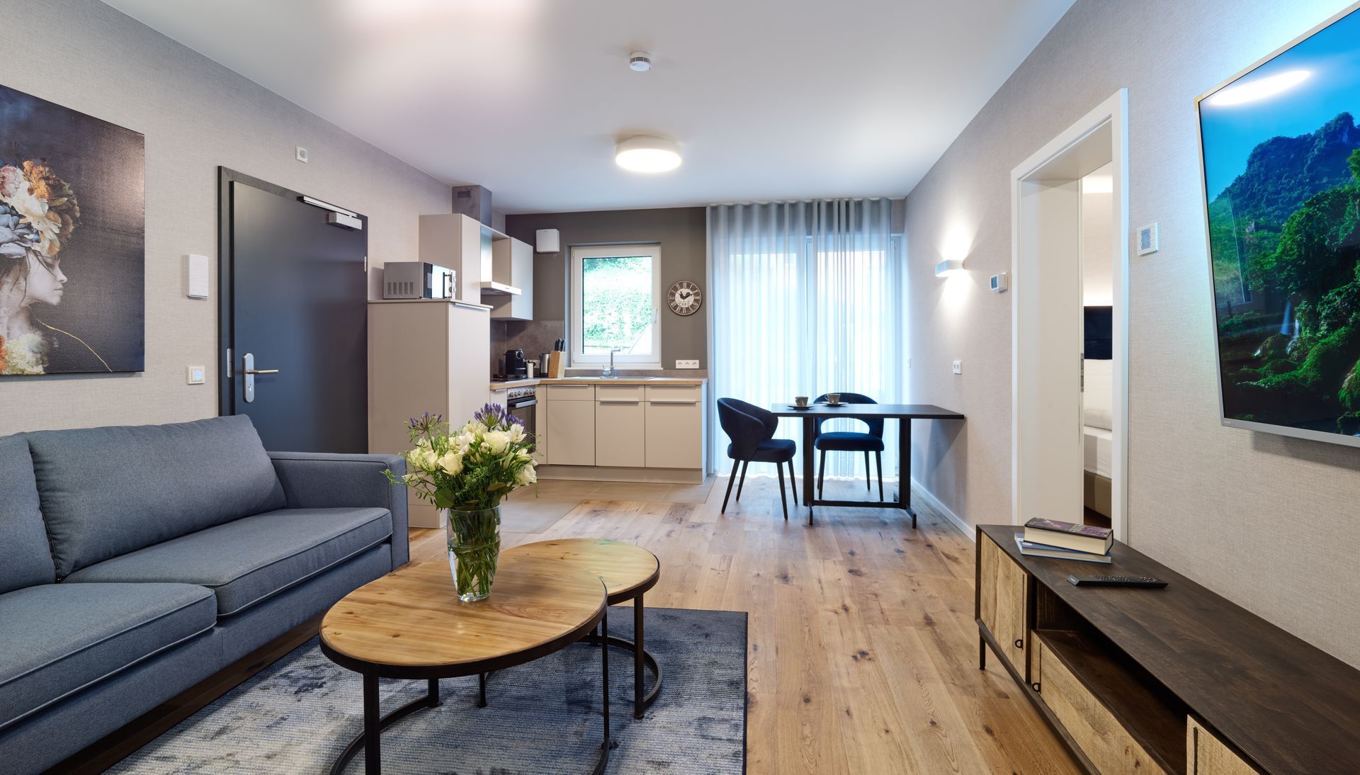 Modernes Wohnzimmer mit grauem Sofa, Couchtisch, Essbereich und großen Fenstern mit Blick auf eine helle Aussicht
