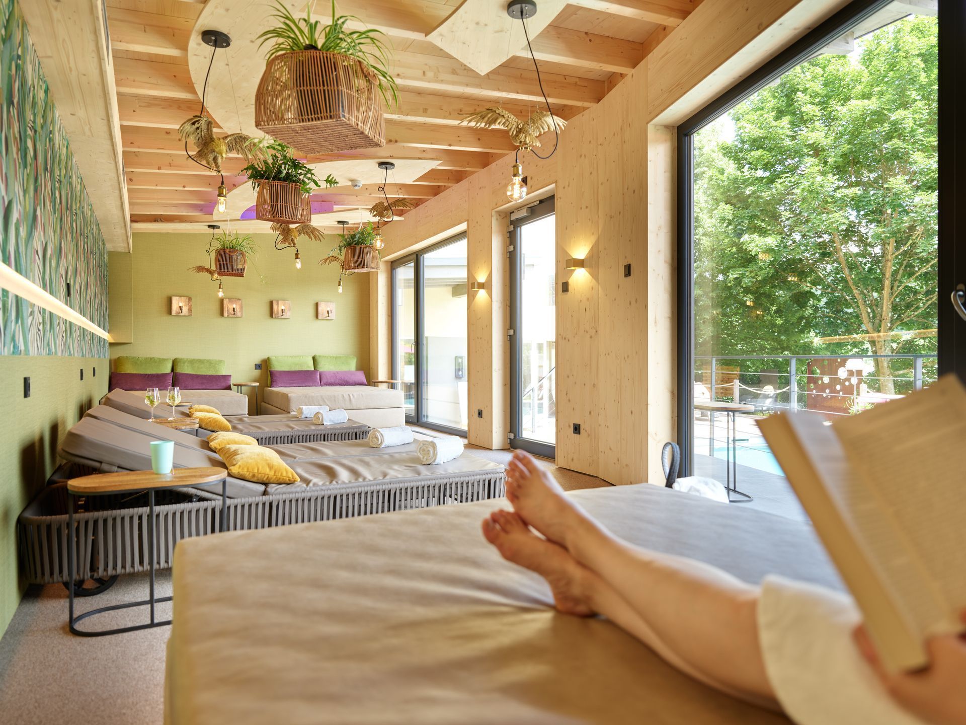 Gemütliche, sonnendurchflutete Lounge mit Betten, Hängepflanzen und großen Fenstern; die Füße hochgelegt im Vordergrund.