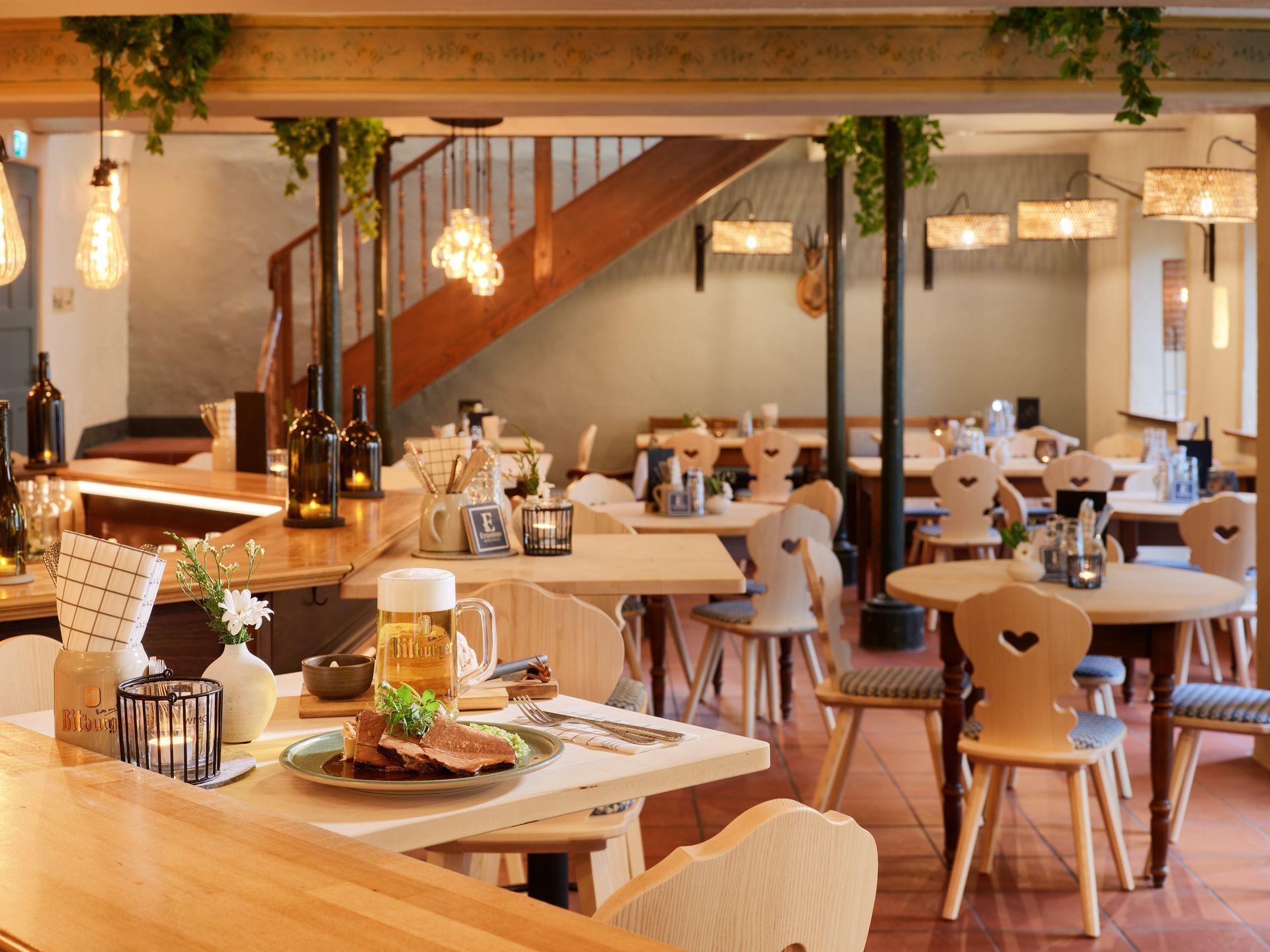 Gemütliches, modernes Restaurantinterieur mit Holztischen, Hängelampen und einer Treppe im Hintergrund