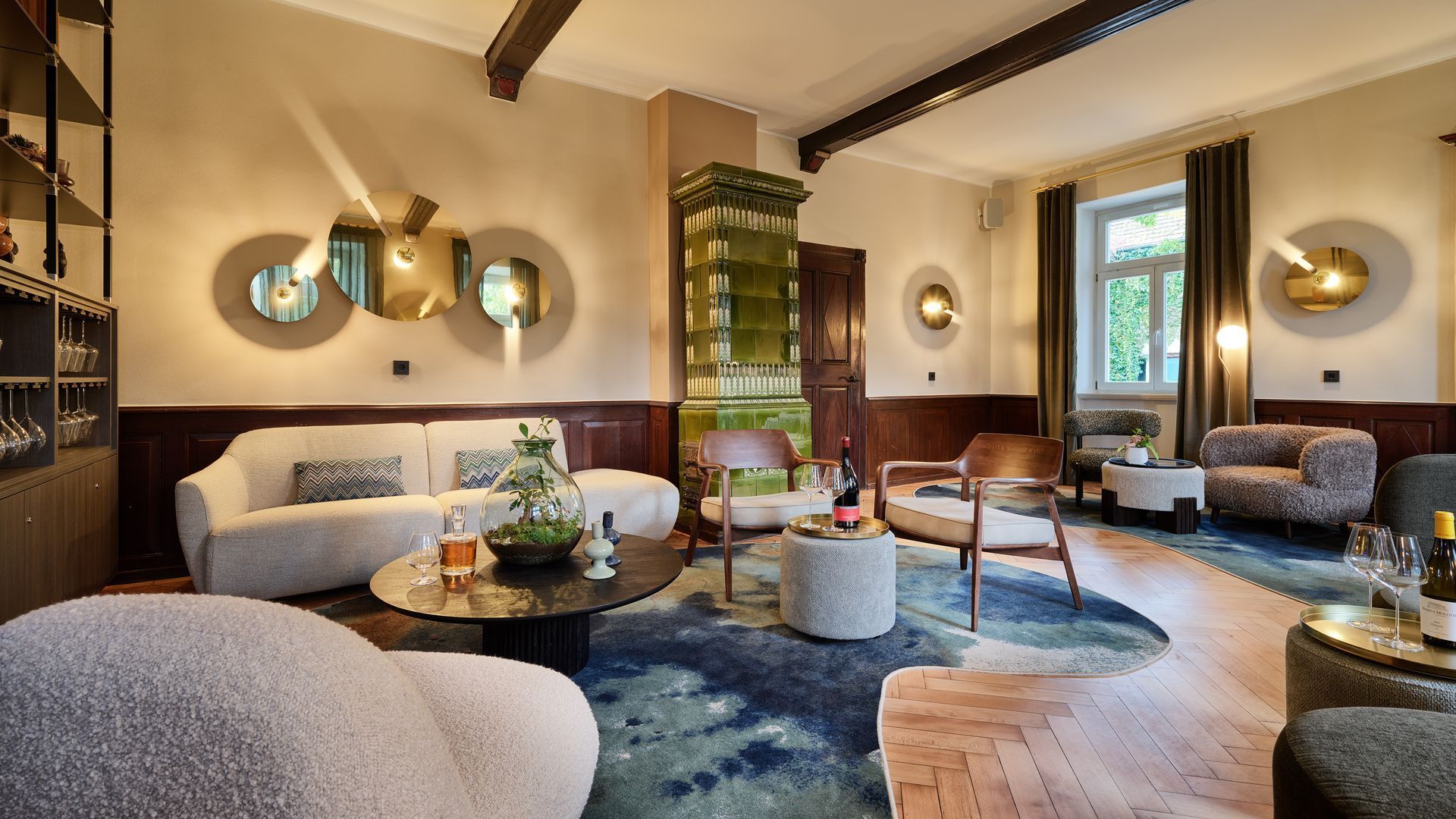 Stilvolles Wohnzimmer mit blauem Teppich, weißen Sofas, runden Couchtischen und Messing-Wanddekoration am Fenster